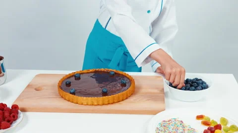 Young chef baker decorating chocolate cake with fruits blueberries on white 動画素材 67259100