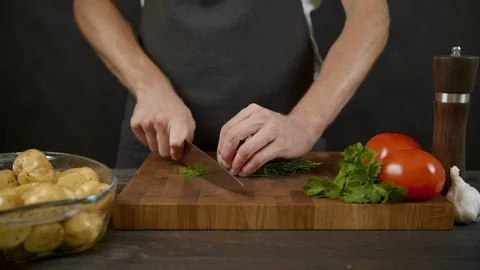 Young chef cutting greens in the isolated dark kitchen Stock Footage 112738066