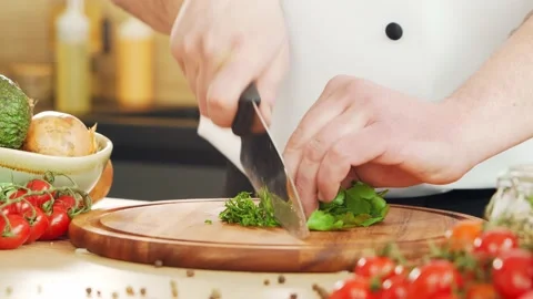 Young chef is cutting herbs and parsley in a modern kitchen. The man prepares Stock Footage 153105433
