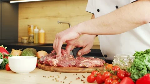 Young chef is cutting meat in a modern kitchen. The man prepares food at home Stock Footage 153036276