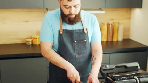 Young chef is cutting meat in a modern kitchen. The man prepares food at home Stock Footage 154386326