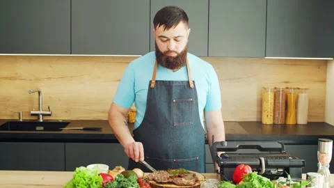 Young chef preparing grilled meat steak in a modern kitchen. The man prepares Stock Footage 154338094