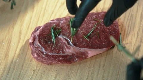 Young chef sprinkles beef steak with rosemary in kitchen of restaurant. Stock Footage 88571605