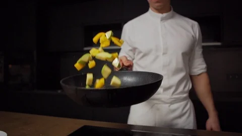 Young chef tossing vegetables in pan over stove Stock Footage 125491275