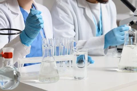 Young chemists dropping water sample into test tubes at table in laboratory,  Stock Photos