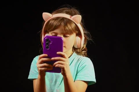 Young child absorbed in a smartphone while wearing playful headphones Stock Photos