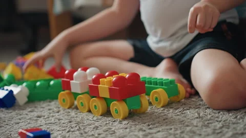 Young child assembles vibrant toy train carefully. Little boy meticulously puts Stock Footage 337725513
