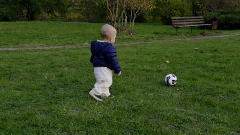 Young child in blue jacket stands on grass, holding a soccer ball, then walks Stock Footage 327851721