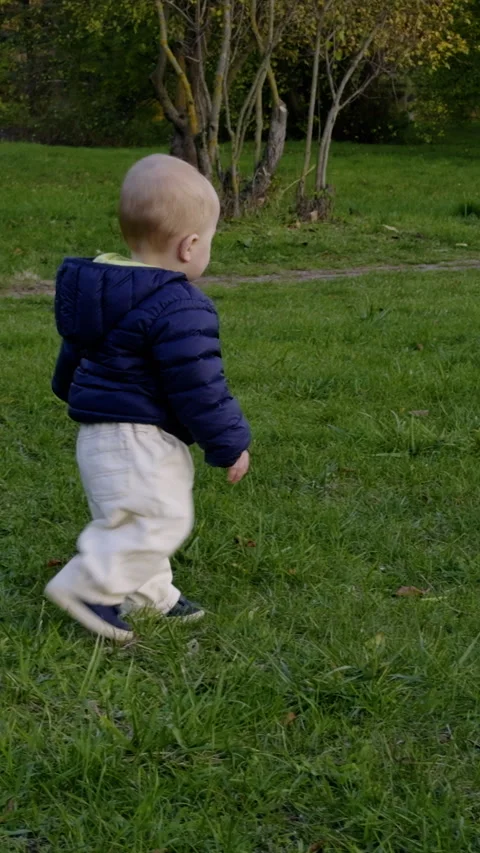 Young child in blue jacket stands on grass, holding a soccer ball, then walks Vídeo Stock 331153754