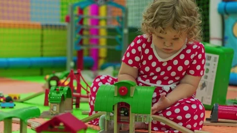 A young child in bright polka dot pajamas builds with a wooden train set in a Video stock 313697745