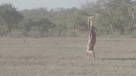 Young child carrying jug on head across field Stock Footage