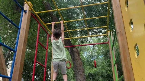 Young child climbing and playing on monkey bars at an outdoor playground. Active Stock Footage 346689415