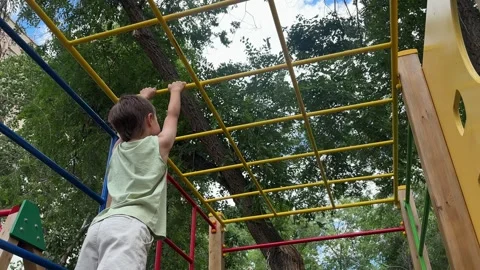 Young child climbing and playing on monkey bars at an outdoor playground. Active Stock Footage 346811169