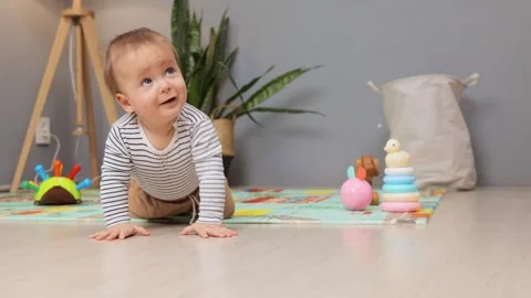 A young child crawls across a bright play mat filled with toys in a comfortable Stockbeeldmateriaal 299938832