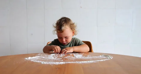 Young child curiously explores flour scattered on kitchen table Stock Footage 248502868