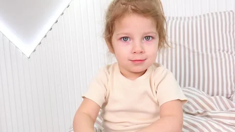 Young child deep in thought while seated on a striped bed Vídeos de archivo 295350377