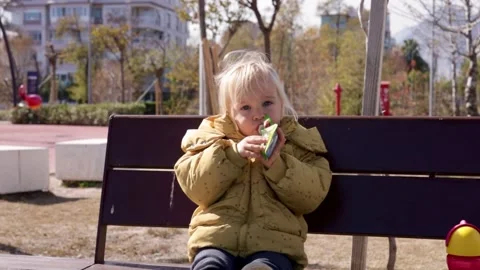 Young child eats fruit snack in park on sunny day, enjoying outdoor fun with Stock Footage 314064225