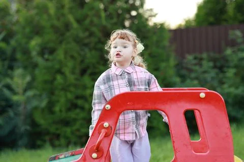 A young child explores a red structure in a grassy yard. The sun sets in the  Stock Photos