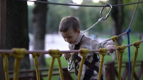 A young child explores a rope obstacle course in a safety harness, reaching Video stock 345936760
