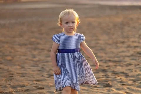 Young child exploring sandy beach during golden hour, showcasing innocence .. Stock Photos