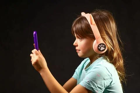 Young child focused on a smartphone while wearing playful wireless headphones Stock Photos