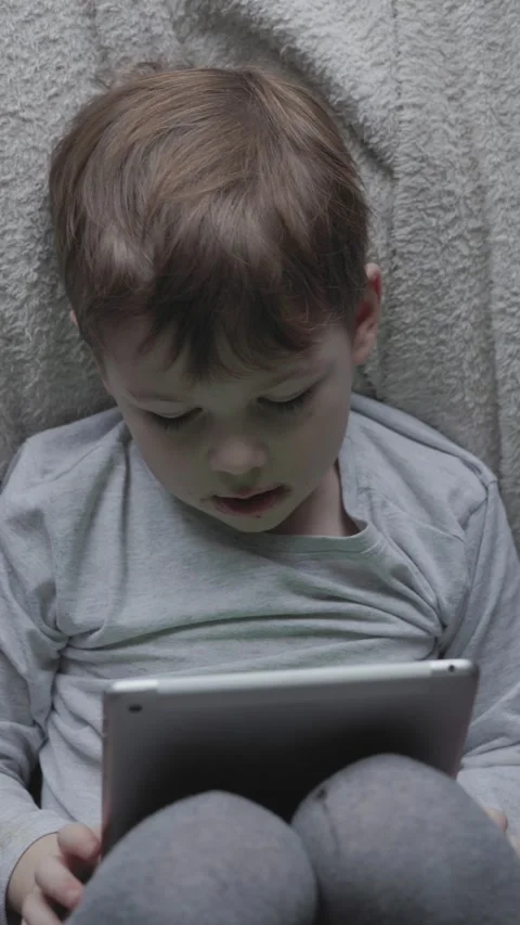Young child focused on tablet in cozy indoor setting during a quiet afternoon Stock Footage 297076897