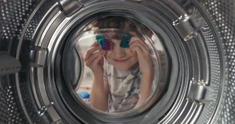 A young child fools around playing by the washing machine. He covers his eyes Stock Footage 200850640