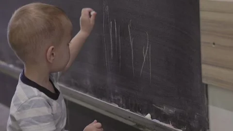 A young child is happily learning to write letters on a chalkboard as part of Stock Footage 314709280