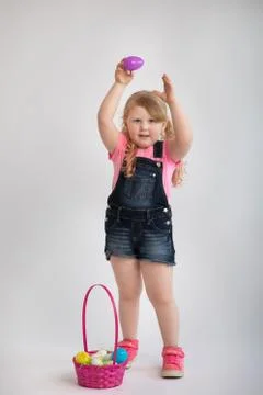 Young child holding up an Easter egg in the air smiling with pink holiday basket Stock Photos