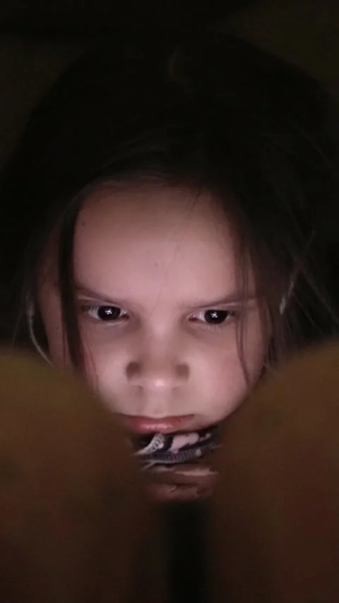 A young child intently using a device with headphones in a dim environment Video stock 308588676