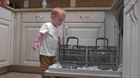 Young child interacts with open dishwasher, showcasing curiosity and early Video stock 291621365