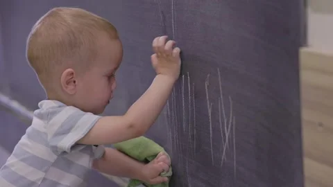A young child joyfully drawing creative pictures on a chalkboard covered with a Video stock 314709264