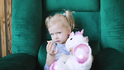 Young child joyfully playing with a stuffed unicorn while enjoying a snack in a Stock Footage 308490241