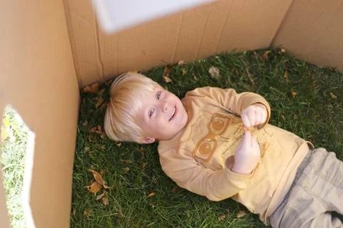 Young Child Laying in Grass while Playing in Cardboard Box Fort Stock Photos