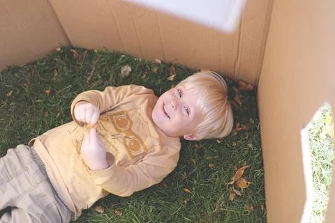 Young Child Laying in Grass while Playing in Cardboard Box Fort Stock Photos