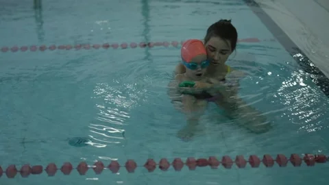A young child is learning to swim with an instructor in a pool, focusing on Video stock 314709365