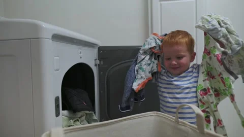 Young child placing clothes into front-load washing machine from a large laundry Stockbeeldmateriaal 320089443