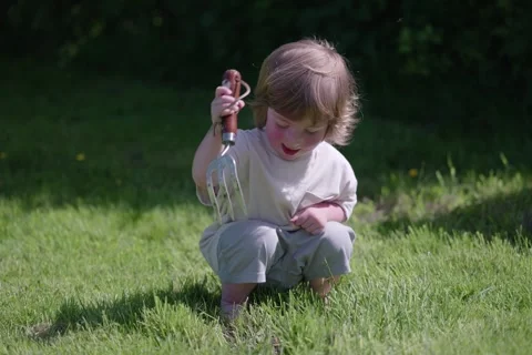 Young Child Playing with Garden Hand Fork Digging in Grass Outdoors 4K Stock Footage 335704624