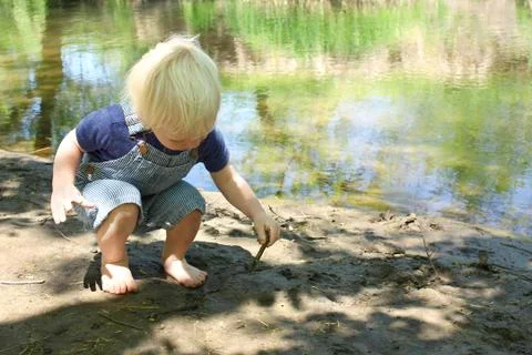Young child playing in mud by river Stock Photos