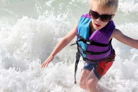 Young child playing in ocean waves in life jacket Stock Photos