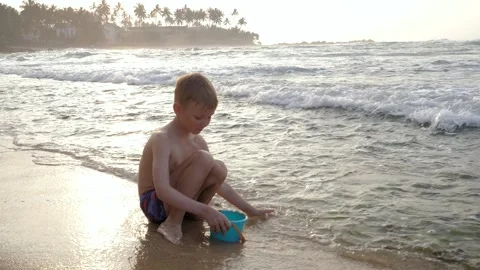 Young child playing with sand and waves on tropical beach at sunset Stock Footage 308154970