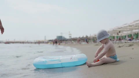 Young child playing on sandy beach with inflatable pool float, scooping sand Stockbeeldmateriaal 340900972