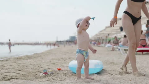 Young child playing on sandy beach with inflatable ring, while adult woman in Stock Footage 341334675