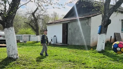 Young child plays with a ball in the yard of a rural house on a sunny day in spr Stock Footage 336227848