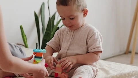 A young child plays with building blocks, focusing on two toys. An adult hand Stockbeeldmateriaal 336459548