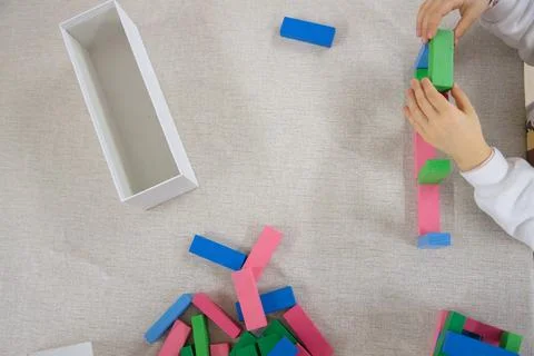A young child plays, focusing while building a structure with wooden blocks Stock Photos