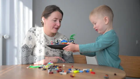 Young child presents construction toy to mom at table, proud of his creation and Stock Footage 346769805