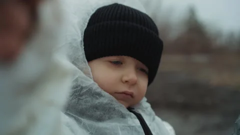 Young child in protective attire amid barren terrain landscape. Juvenile Stock Footage 346460834