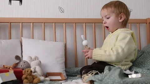 A young child sits on a bed, assembling a wooden stacking toy in the shape of a Stock Footage 290768689