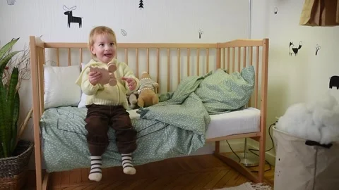 A young child sits on a bed, playing with a wooden toy in a cozy bedroom. The Stock Footage 290586533
